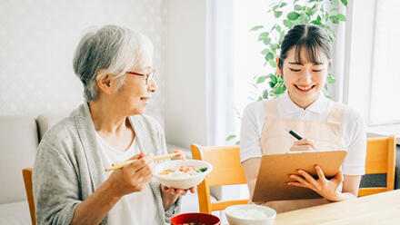 食事中の高齢者に寄り添う女性